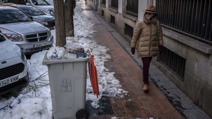 Una mujer pasa junto a un cubo de basura en la calle Lagasca,