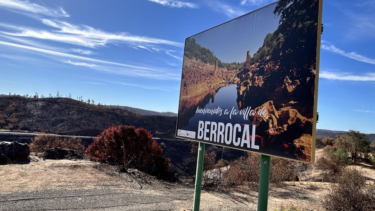 Cartel que anuncia la llegada a Berrocal, ante unas montañas arrasadas por el fuego.