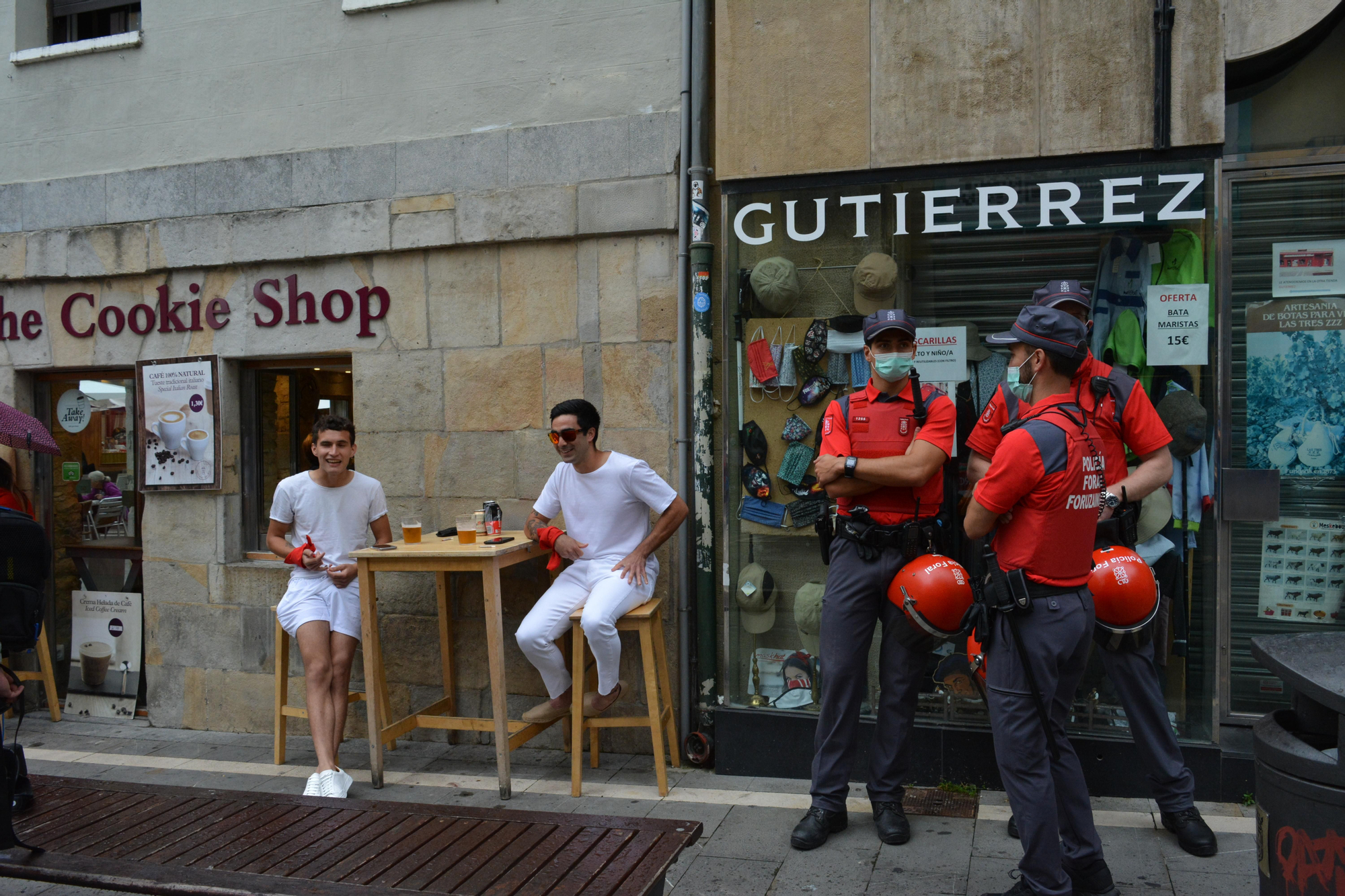 Dos personas vestidas de blanco y rojo sentados en una cafetería al lado de un control de la Policía Foral