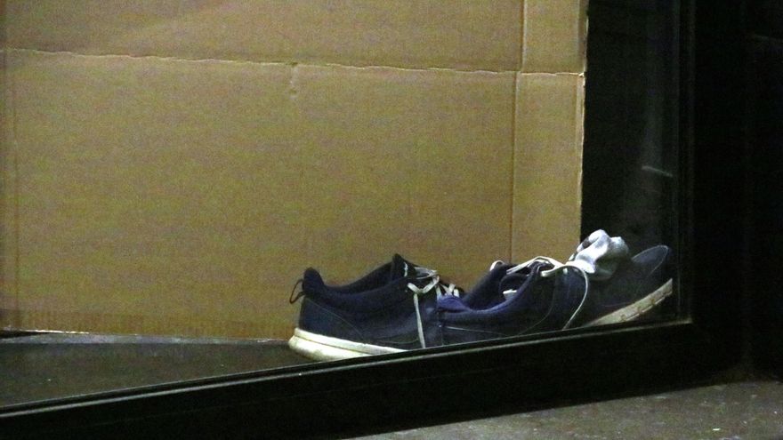 Unas zapatillas y un cartón en un cajero de Barcelona donde vive una persona sin hogar
