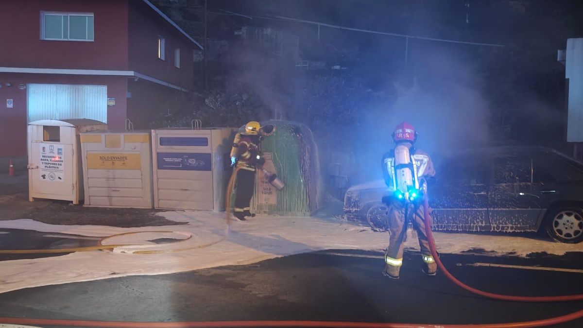 Dos bomberos apagando el incendio en un vehículo  estacionado en la carretera de Hoyo de Mazo.