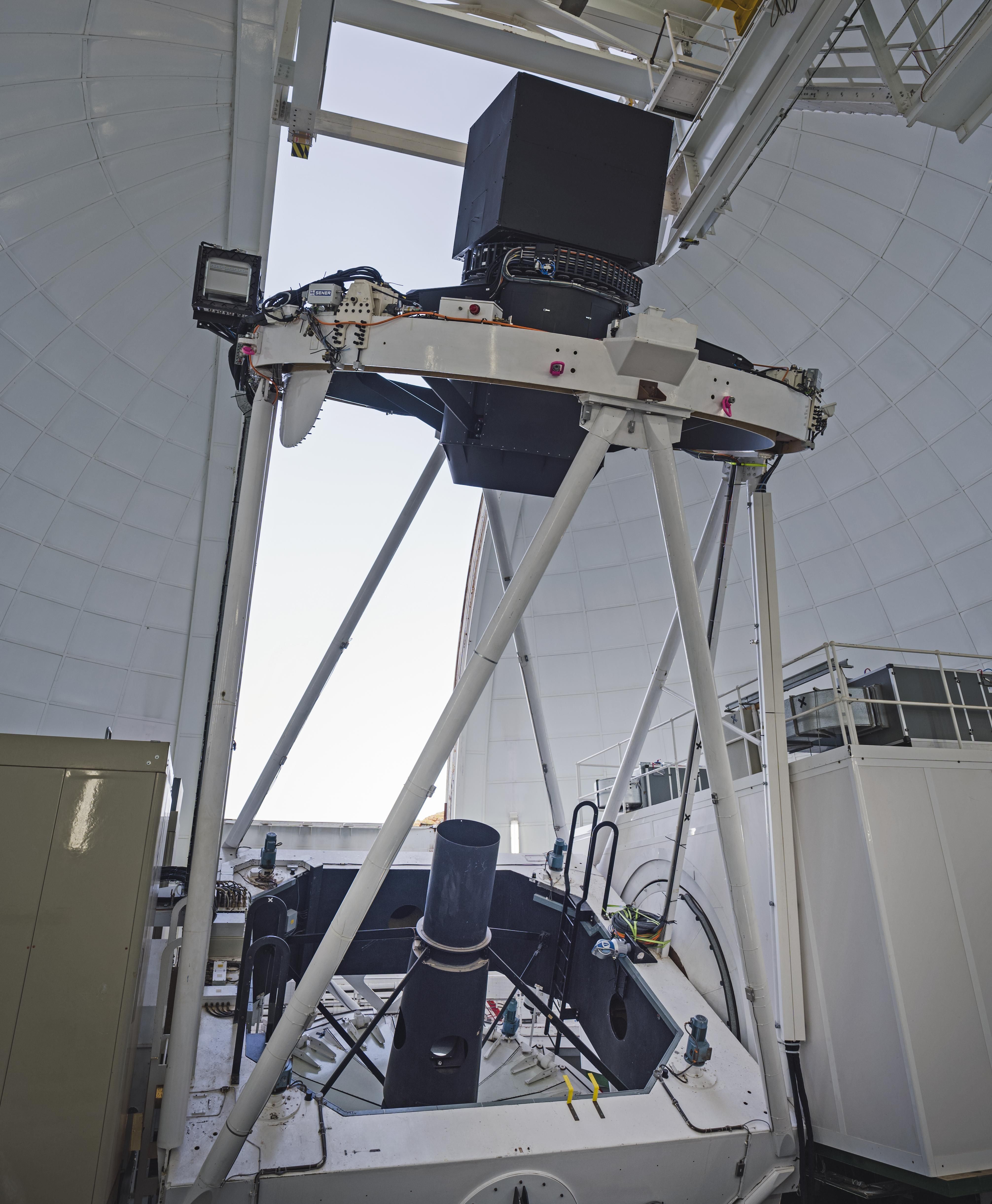 El Telescopio William Herschel con WEAVE. El posicionador WEAVE está alojado en la caja negra de 1,8 metros sobre el anillo superior. Las fibras ópticas recorren la estructura del telescopio hasta el recinto de la izquierda, que alberga el espectrógrafo WEAVE. Crédito: Sebastián Kramer.