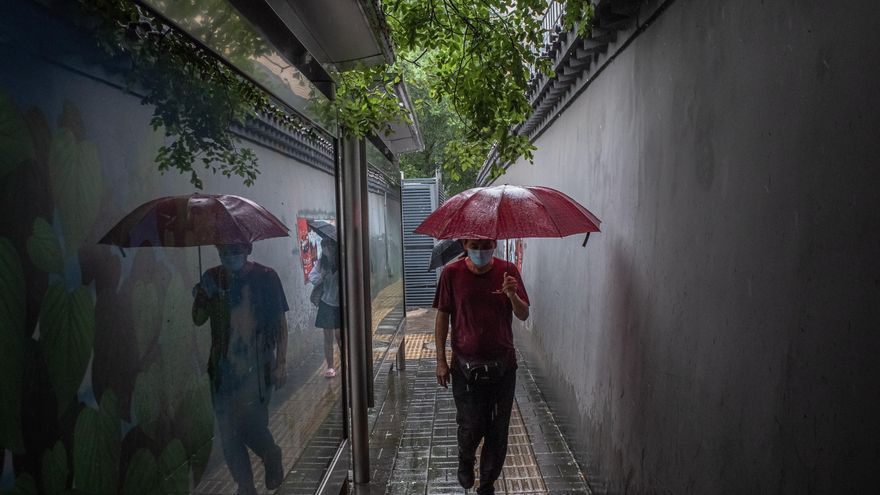 Un hombre con mascarilla camina con un paraguas bajo la lluvia en Pekín, China. EFE/ROMAN PILIPEY
