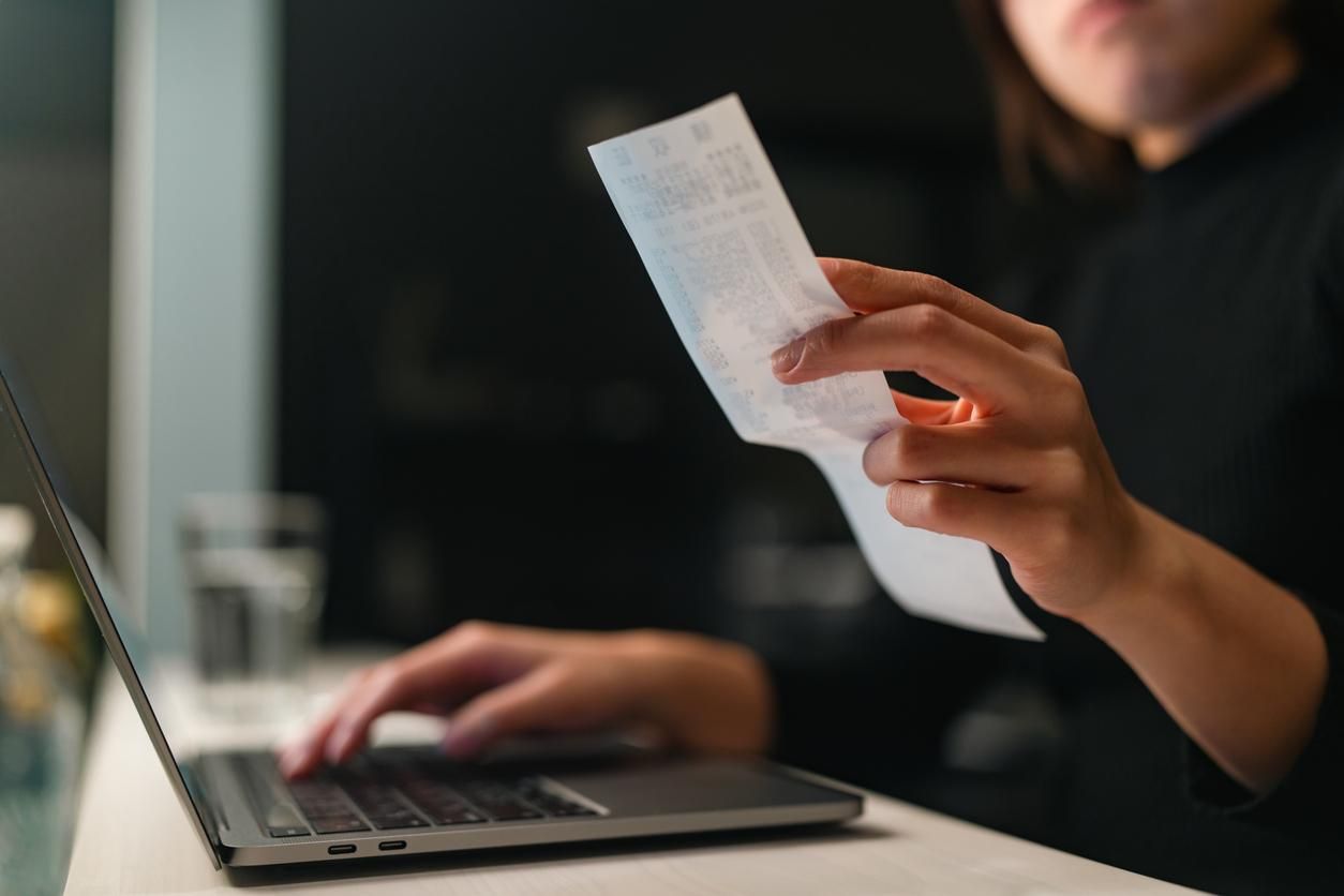 Primer plano de una persona introduciendo datos de un ticket de compra en un ordenador portátil para la contabilidad de su empresa.
