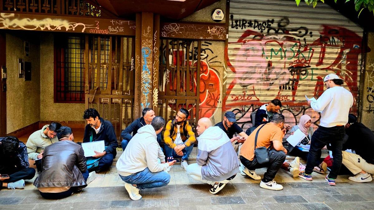 Algunas personas se sientan frente al Ayuntamiento de València mientras rellenan los formularios para la regularización.