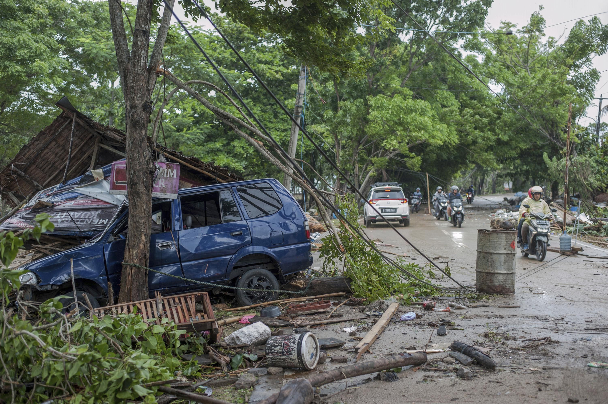 Varios motoristas circulan cerca de un coche arrastrado por el tsunami en Carita, Indonesia