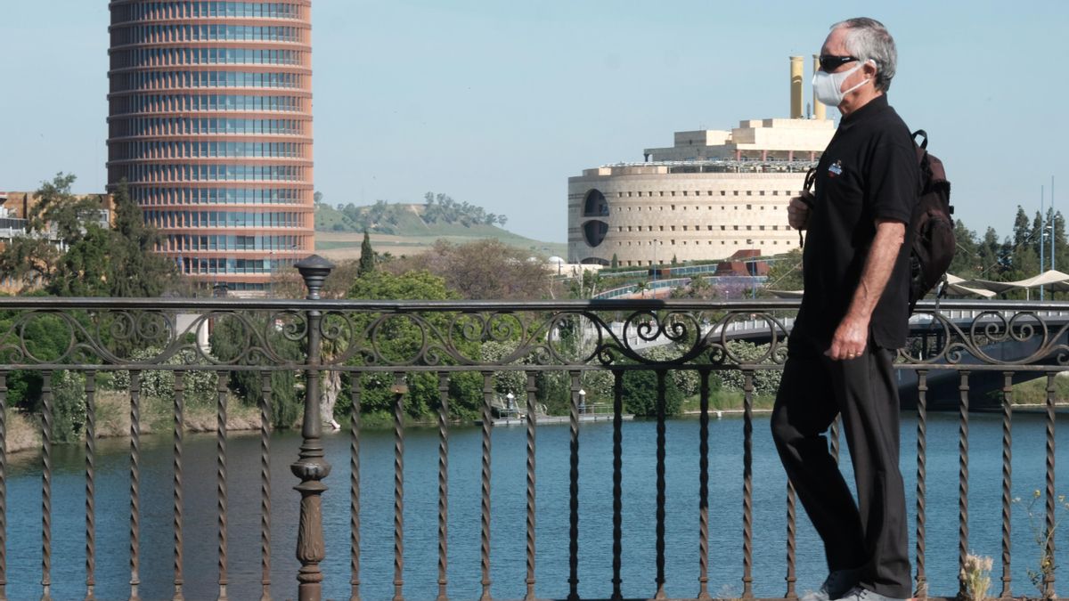 Una persona protegida con mascarilla pasea por el puente de Triana.