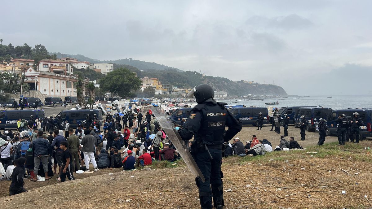 Decenas de personas migrantes aguardan el operativo policial desplegado en la Playa del Trampolín, en Ceuta