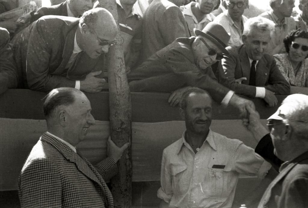 Espectadores, probablemente autoridades, detrás de una bandera de España