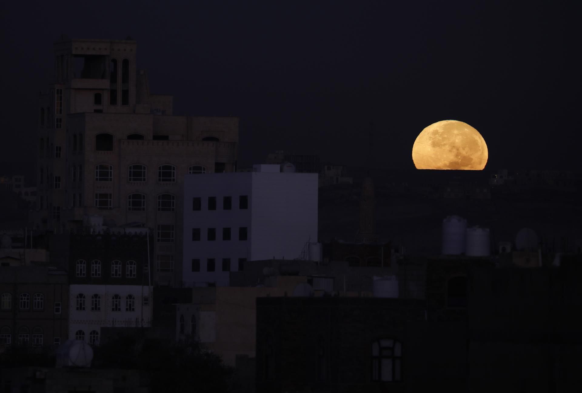 La luna llena se esconde tras unos edificios en la ciudad de Sana'a, en Yemen.
