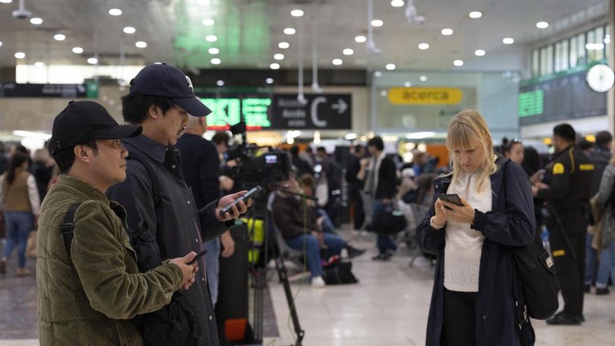 Varios pasajeros miran el móvil y esperan en la Estación de Sants de Barcelona este lunes