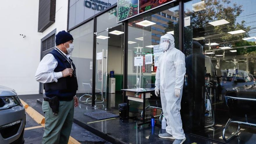 Un guardia de seguridad y un hombre, parte del personal sanitario, usan implementos para protegerse del coronavirus en un local de cambio de dinero, este lunes, en Asunción (Paraguay).