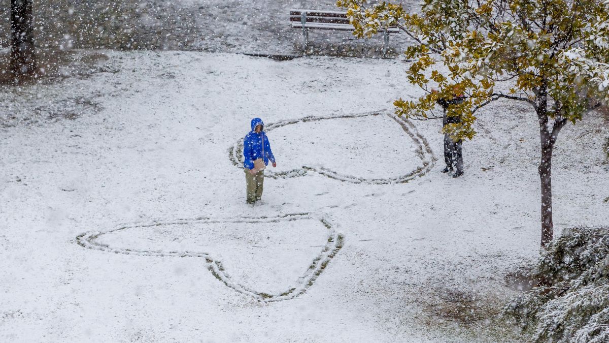 Dos personas caminan bajo la nieve que ha empezado a caer a media mañana hoy viernes en Zaragoza.