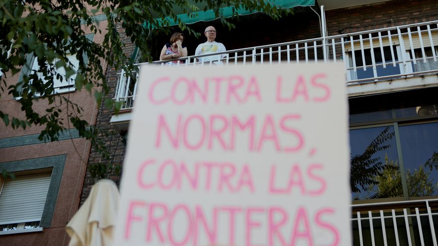 "Contra las normas, contra las fronteras": uno de los carteles de la protesta observada por una pareja desde el balcón