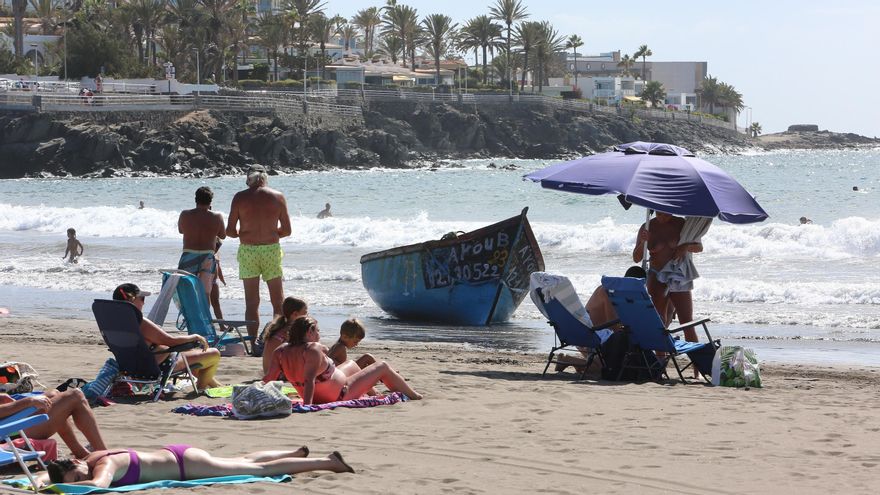 Veraneantes al lado de una patera llegada a la Playa de Las Burras, en el sur de Gran Canaria, con al menos seis personas a bordo.