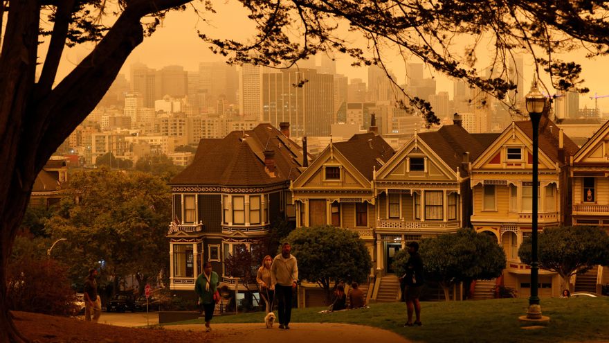 Gente reunida en Alamo Square bajo un cielo nublado naranja con vistas a The Painted Ladies, la icónica fila de casas victorianas en San Francisco