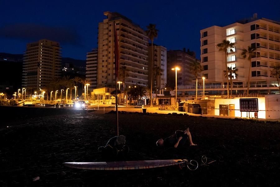 Un hombre realiza estiramientos antes de meterse en el agua para hacer surf en el Puerto de la Cruz (Efe / Miguel Barreto)