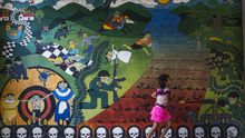Una niña camina junto a uno de los murales que recuerdan el conflicto armado interno de El Salvador en Carasque