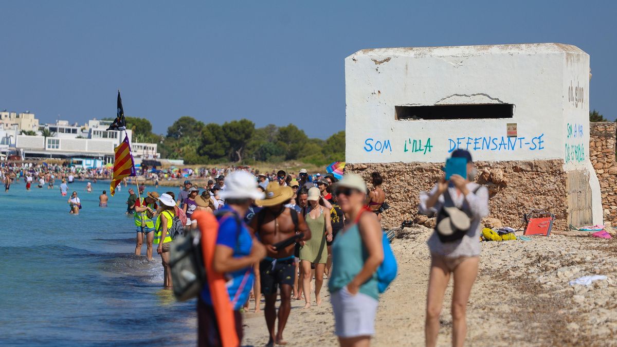 Los manifestantes ocupan la playa de es Trenc. Detrás, una de las infraestructuras defensivas instaladas con el siguiente mensaje en catalán: "Somos la isla defendiéndose".