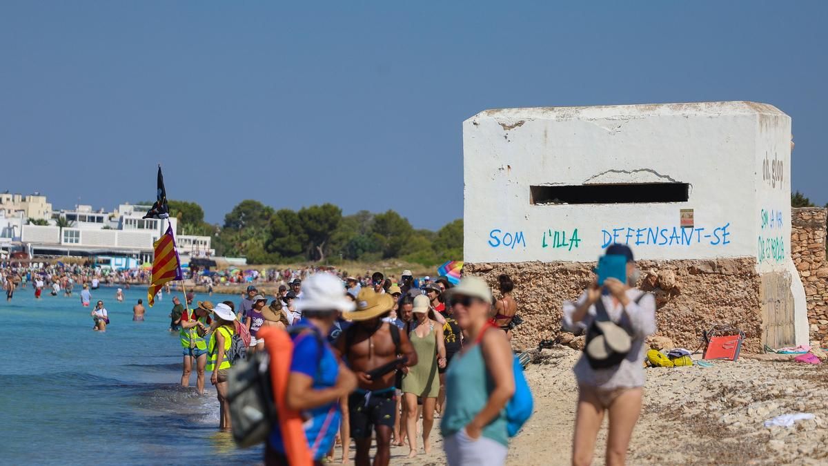 Los manifestantes ocupan la playa de es Trenc. Detrás, una de las infraestructuras defensivas instaladas durante la II Guerra Mundial con el siguiente mensaje en catalán: "Somos la isla defendiéndose".
