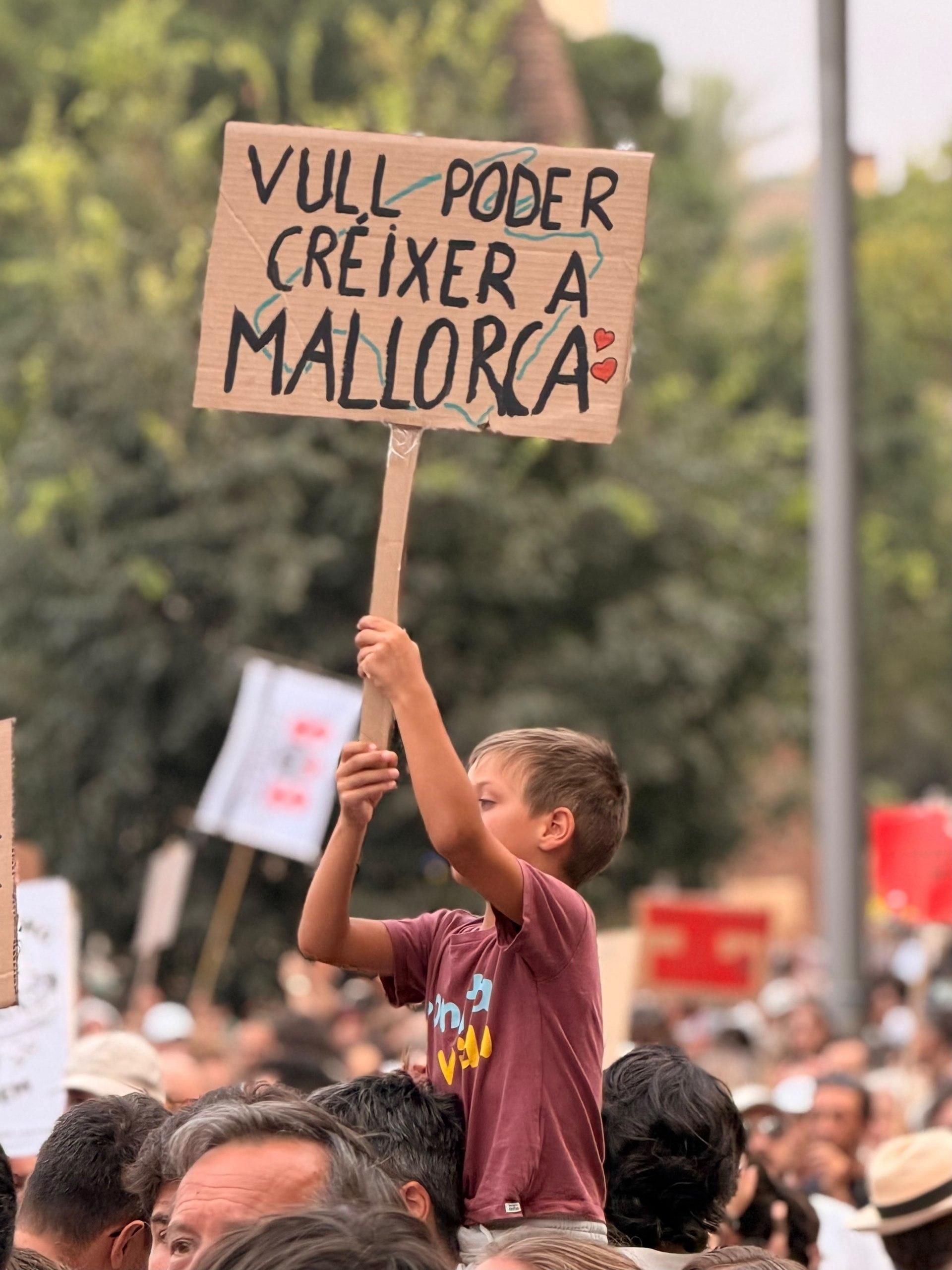 Un nen sosté una pancarta que diu en català: "Vull poder créixer a Mallorca"