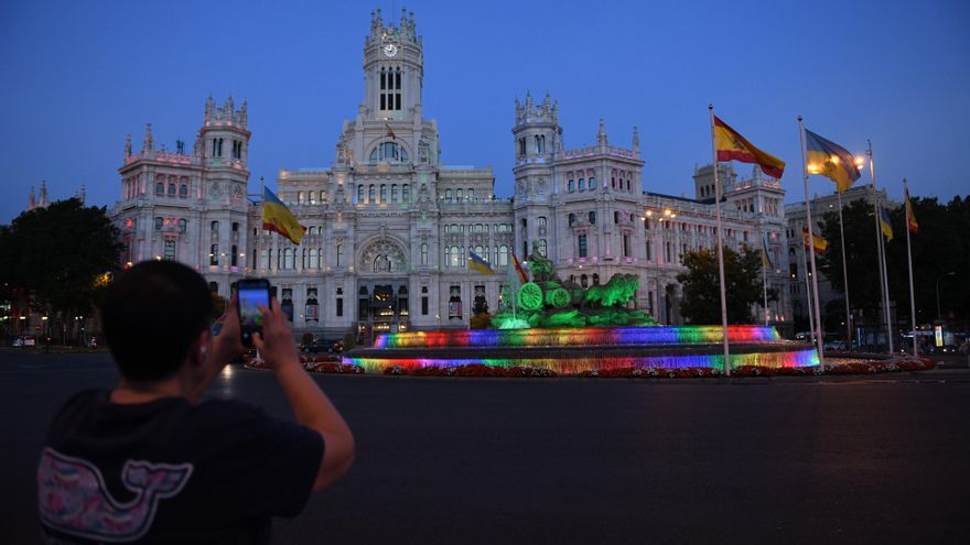 Archivo - Una persona fotografía la fuente y el Palacio de Cibeles con los colores de la bandera LGTB