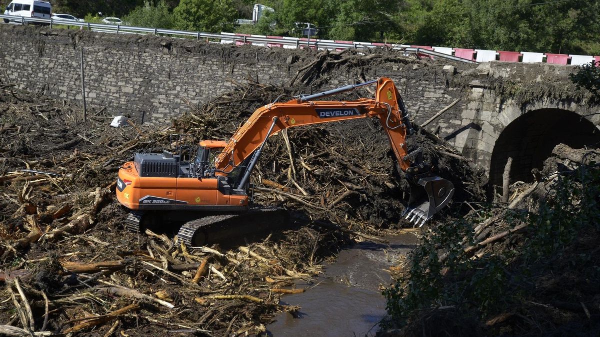 Una excavadora retira restos de árboles y barro acumulados haciendo presión sobre un puente en Pradocabalos (Viana do Bolo, Ourense).