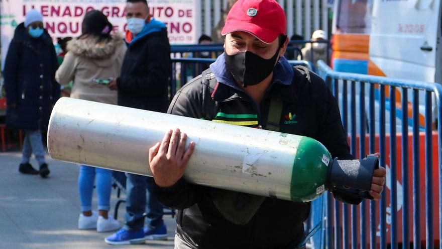 Una persona transporta un tanque de oxígeno mientras otras esperan turno para la carga de oxígeno en la alcaldía de Iztapalapa, en Ciudad de México.