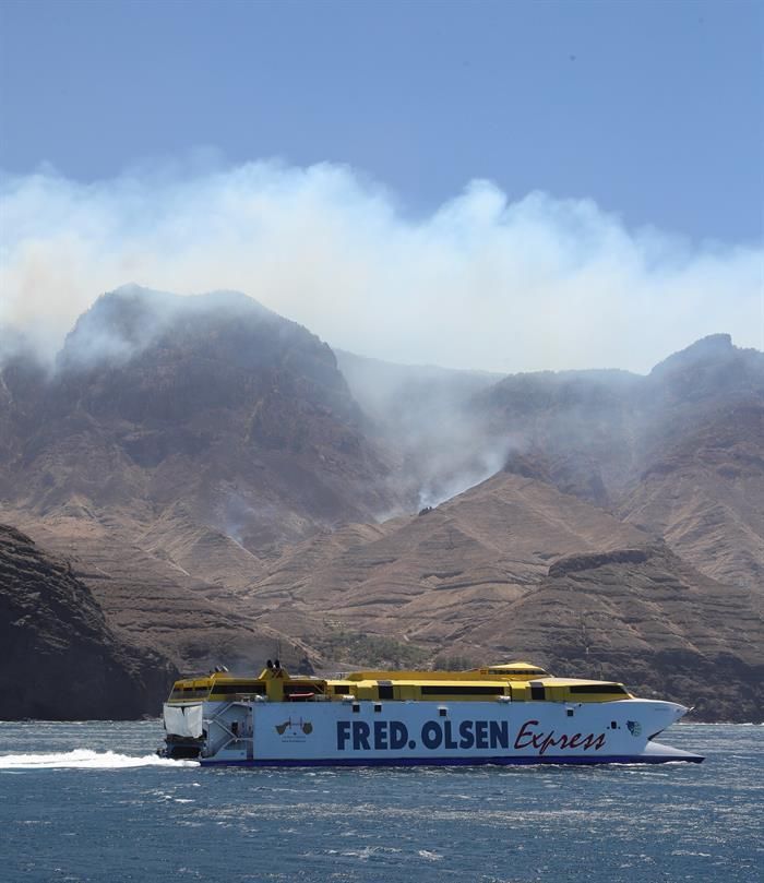 El ferry de Fred Olsen sale del puerto de Las Nieves, en Agete, mientras en lo alto del acantilado sigue activo el foco del incendio de Gran Canaria en el pinar de Tamadaba. EFE/Elvira Urquijo A.