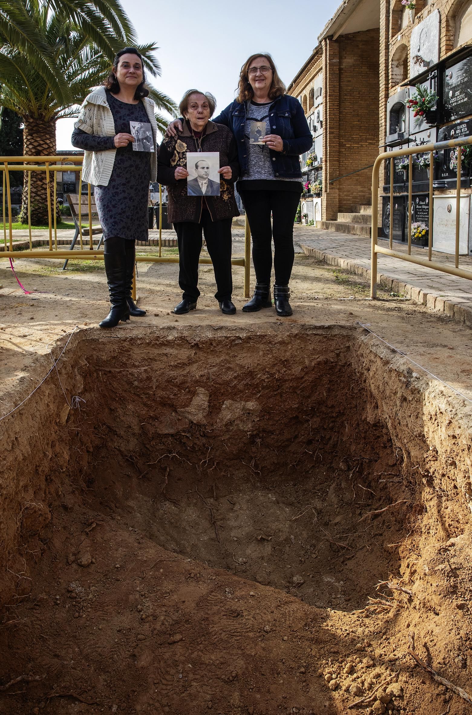Tres mujeres sostienen los retratos de sus seres queridos a pie de fosa en el cementerio de Paterna.