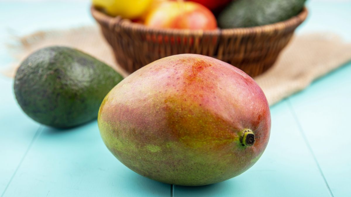 Un delicioso mango frente a una cesta de frutas