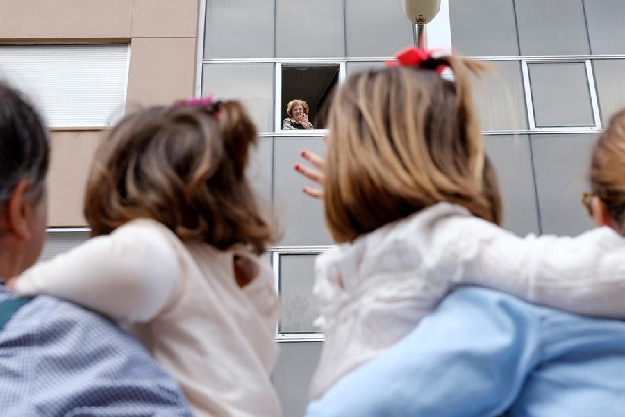 Niñas saludan a sus vecinos desde la calle en el primer día en que pueden salir
