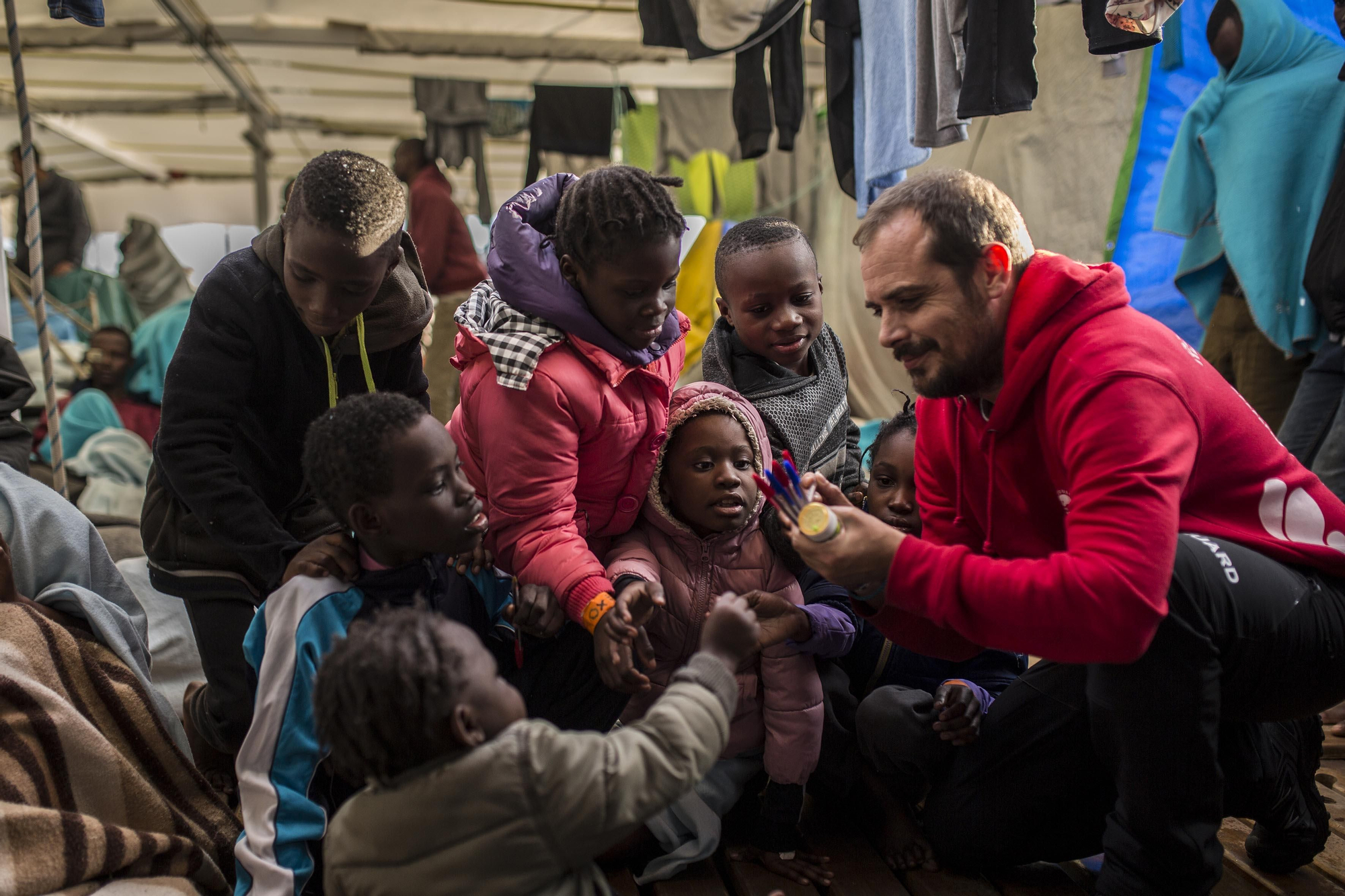 Marc, capitán del Open Arms durante la misión 57 de la ONG, reparte bolígrafos y papeles a algunos de los niños rescatados para que puedan dibujar / Olmo Calvo
