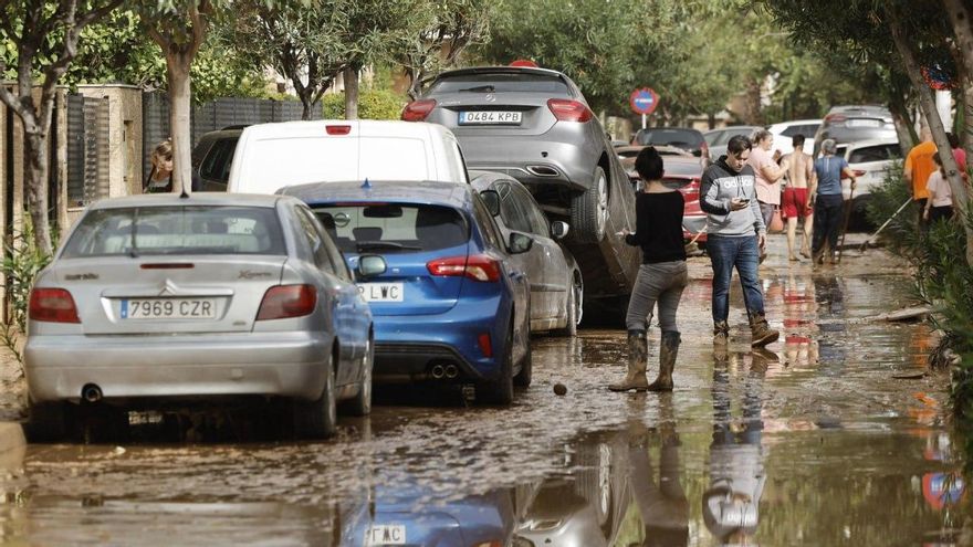 Varias personas junto a vehículos dañados por las intensas lluvias, este miércoles en Picaña (Valencia).