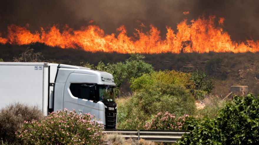 Un camión circula por la autopista A7 con las llamas del incendio forestal de Los Gallardos de fondo.