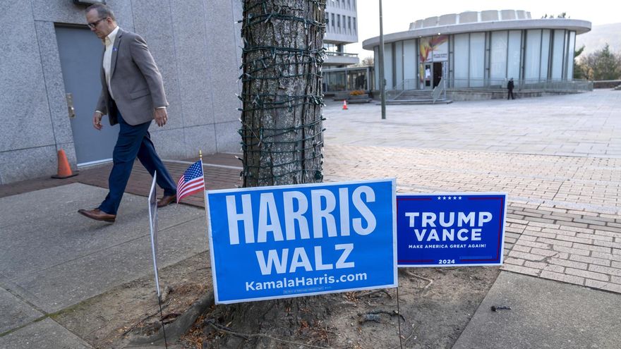 Un hombre camina frente a unos carteles de los candidatos presidenciales, los demócratas Harris y Walz y los republicanos Trump y Vance, en un centro de votación.