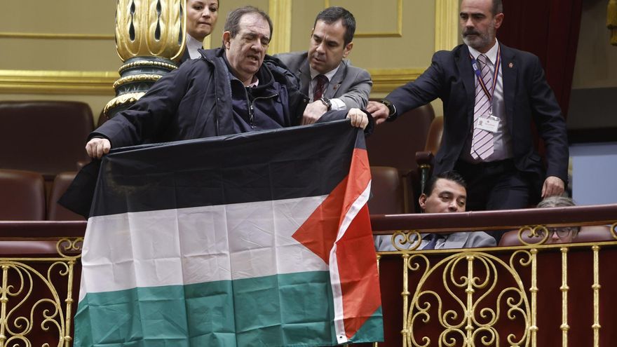 Un asistente despliega una bandera palestina durante el pleno del Congreso en el que comparece el ministro de Asuntos Exteriores, Unión Europea y Cooperación, José Manuel Albares, para informar sobre la situación en Gaza, Israel y Oriente Medio, este martes en Madrid.