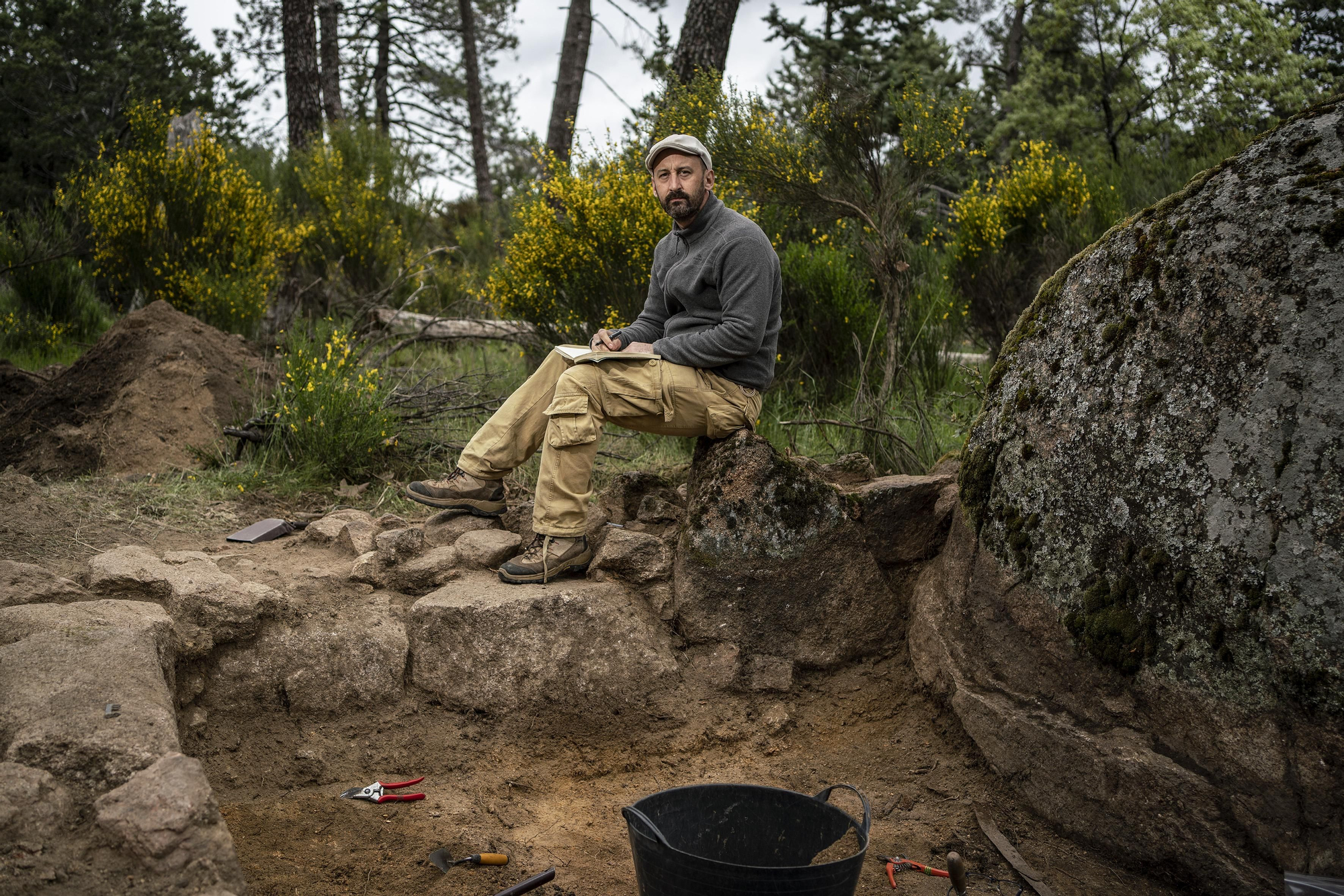 El arqueólogo Alfredo González Ruibal junto a una de las chabolas encontradas, de la que queda en pie su basamento, apoyado en un bolo granítico característico de la zona