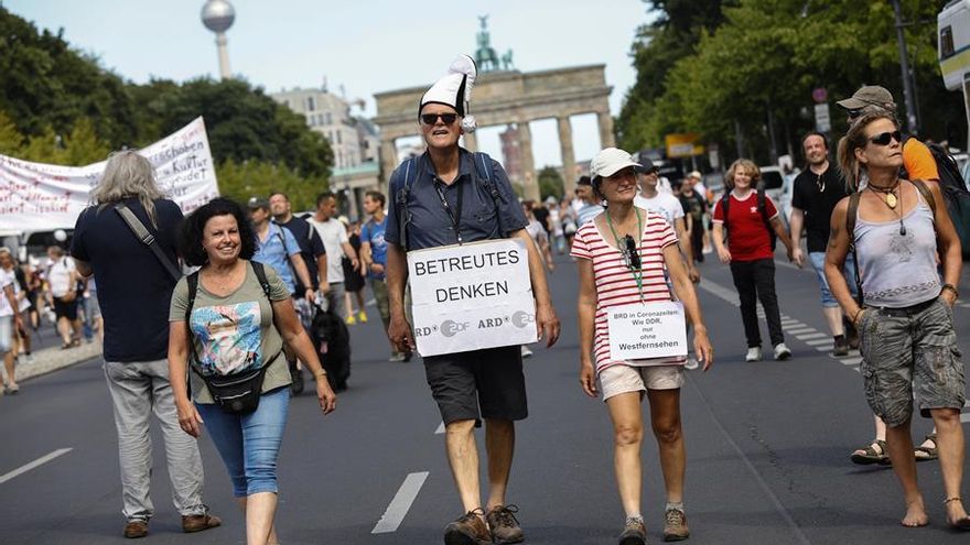 Unos manifestantes caminan frente a la Puerta de Brandenburgo mientras sostienen una cartulina en la que se lee "pensamiento guiado"