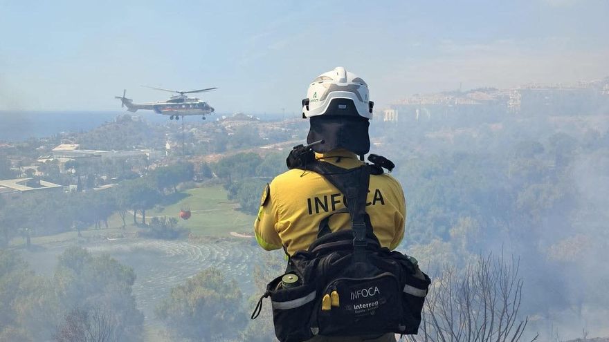 Un operario movilizado por el Plan Infoca contempla las tareas de un helicóptero en la extinción de un incendio en la zona de Santángelo Oeste en la ciudad malagueña de Benalmádena.