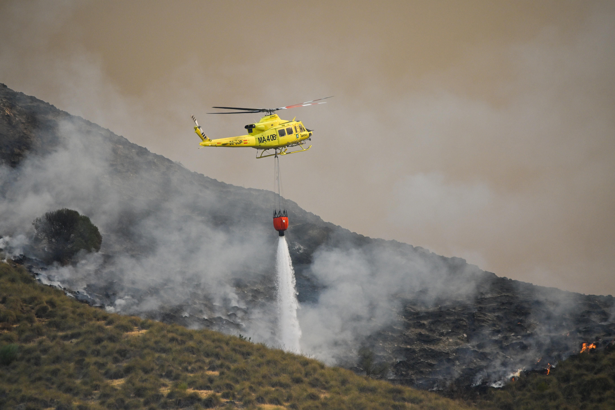 Un helicóptero lanza agua sobre el terreno. EFE | Carlos Barba