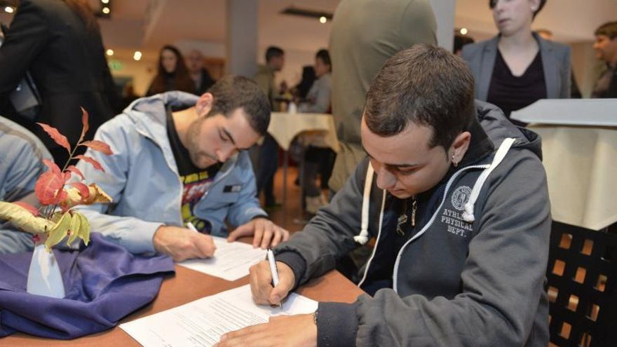 Jóvenes rellenan unos documentos en unas pruebas para irse a trabajar al extranjero.