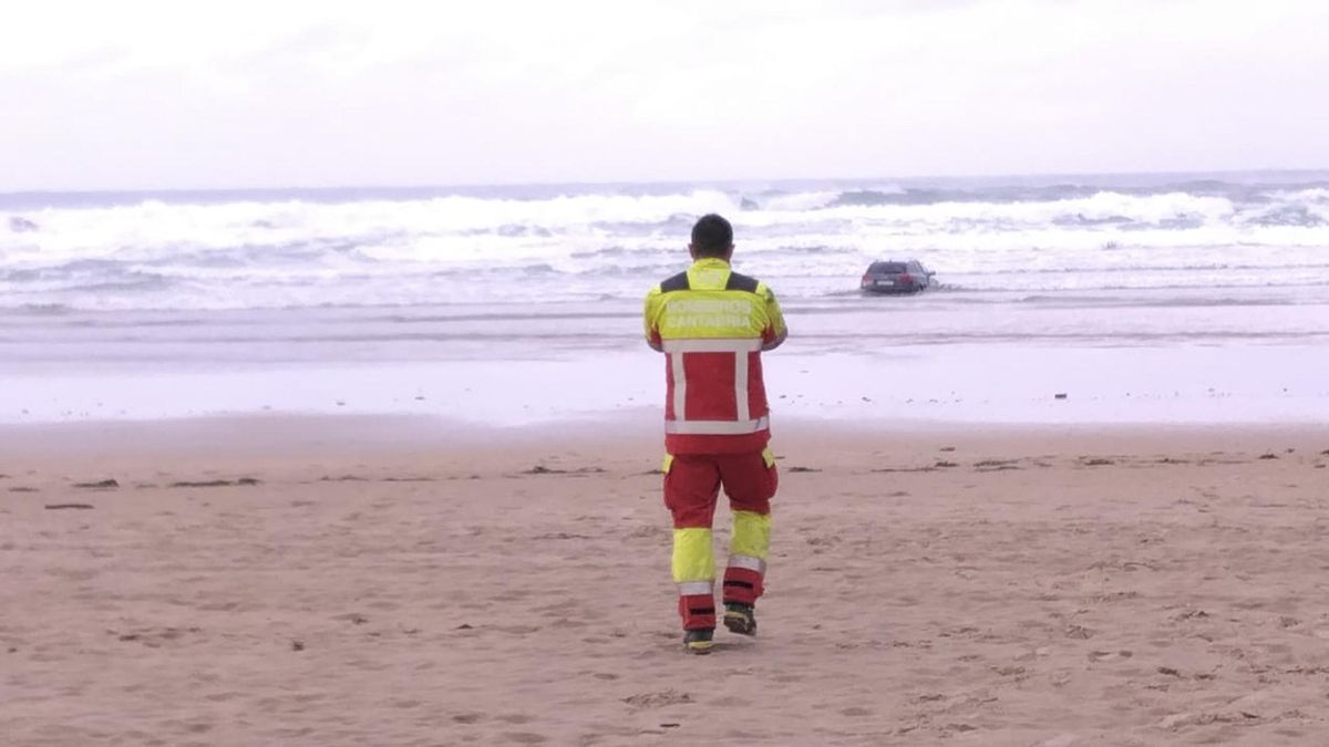 Un efectivo de los Bomberos de Cantabria se dirige hacia un coche encallado, dentro del agua, en la orilla de la playa de Oyambre en Cantabria.