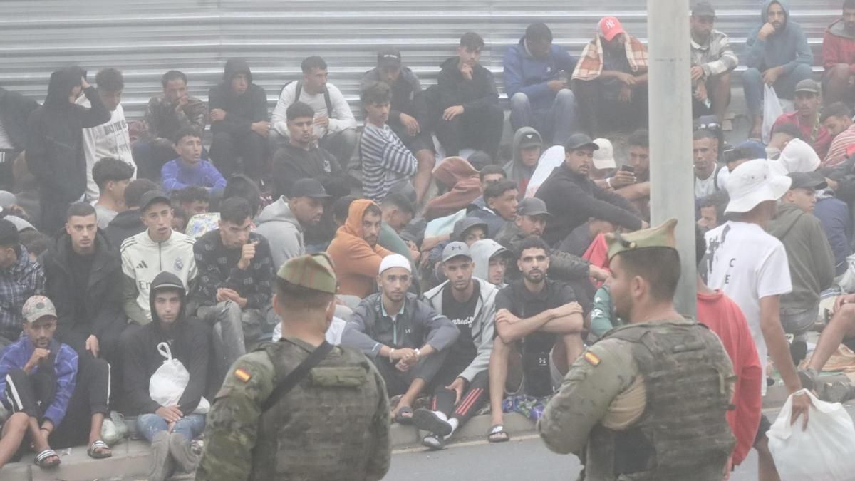 Migrantes concentrados en las inmediaciones de la explanada de embolsamiento de Loma Colmenar de Ceuta este miércoles con la esperanza de conseguir una plaza en un nuevo centro de acogida. EFE/Reduan