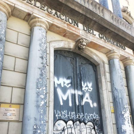 La puerta que da a la calle Marquès de l'Argentería, con un grafiti. Se aprecia la pintura desconchada de las columnas que decoran la pared