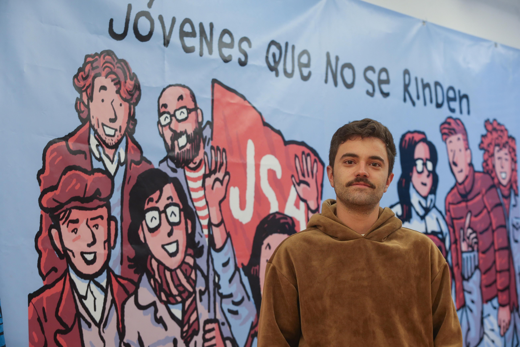 Sergio Llera Suárez, secretario general de Juventudes Socialistas de Asturias, junto al cartel del dibujante Alfonso Zapico. 