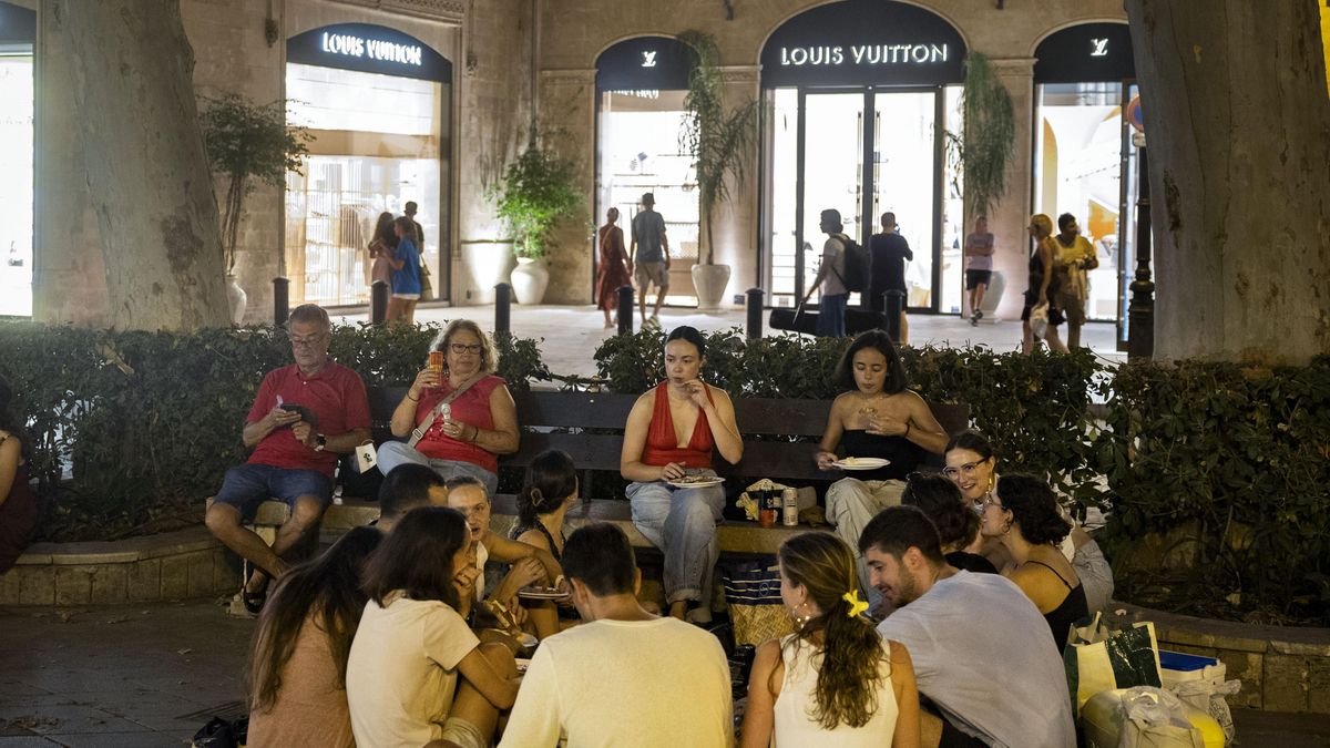 El 'Sopar a la Llesca' se ha celebrado en el Passeig del Born, donde se ubican las tiendas más exclusivas y caras de la ciudad. En la imagen, un grupo de personas cenan frente al negocio de la marca Louis Vuitton.