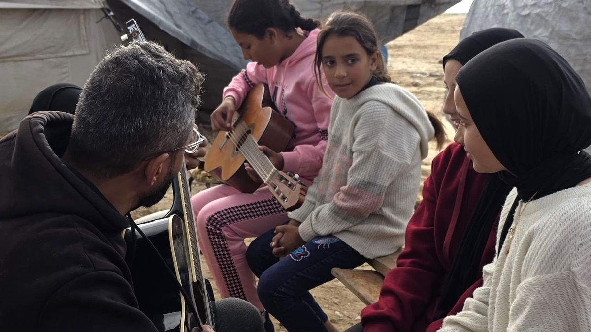 Ahmed Muin Abu Amsha toca la guitarra con algunas alumnas de música en un campo de desplazados de la Franja.