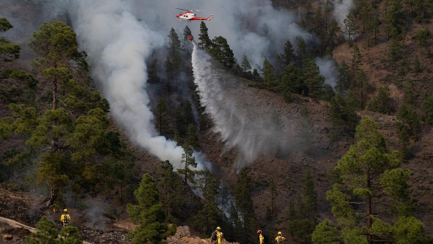 Un helicóptero del Gobierno de Canarias descarga agua sobre una de las zonas del incendio en el municipio de Arico, en el barranco de Tamadaya, donde se están centrando los trabajos para evitar que el fuego avance por el flanco izquierdo. Mientras una brigada de extinción de incendio actúa desde tierra.