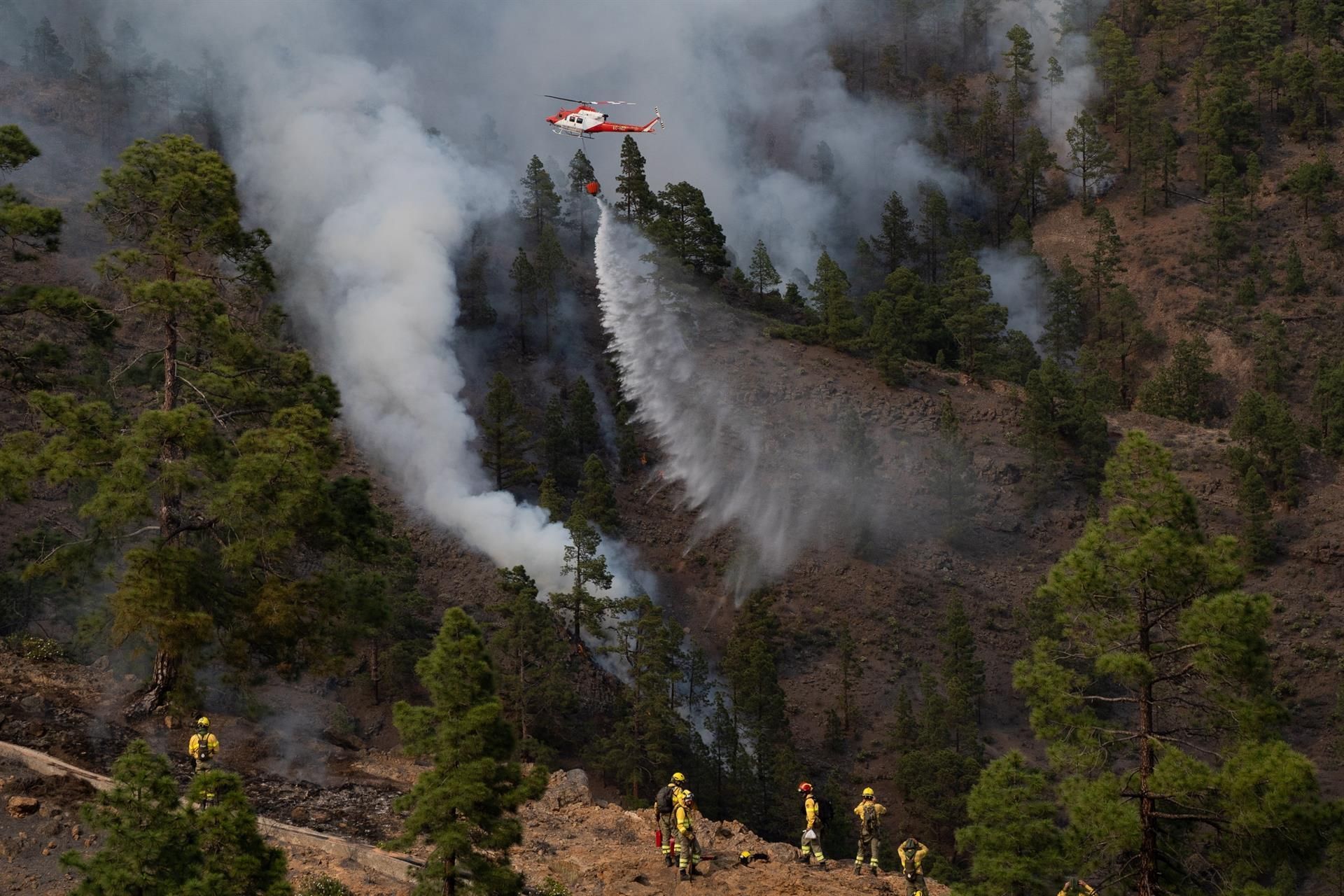 Un helicóptero del Gobierno de Canarias descarga agua sobre una de las zonas del incendio en el municipio de Arico, en el barranco de Tamadaya, donde se están centrando los trabajos para evitar que el fuego avance por el flanco izquierdo. Mientras una brigada de extinción de incendio actúa desde tierra.
